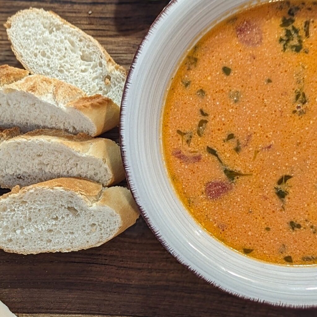 Einladend angerichtete Tomatensuppe, angerrichtet mit frischem Brot und dekoriert mit frischen Kräutern.