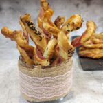 Ein Glas mit mehreren Baconspiralen mit Blätterteig, teilweise mit Schwarzkümmel bestreut.