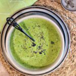 Eine cremige Bärlauch-Cremesuppe in einer weißen Schüssel, garniert mit Kresse-Blättern auf einem rustikalen Tisch.