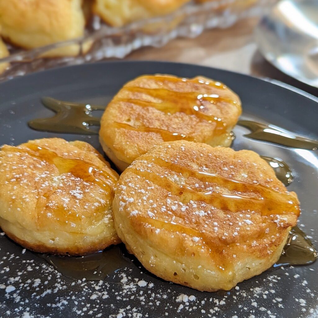 Mehrere Mini-Pfannkuchen Oladji auf einem Teller, mit Honig und Puderzucker
