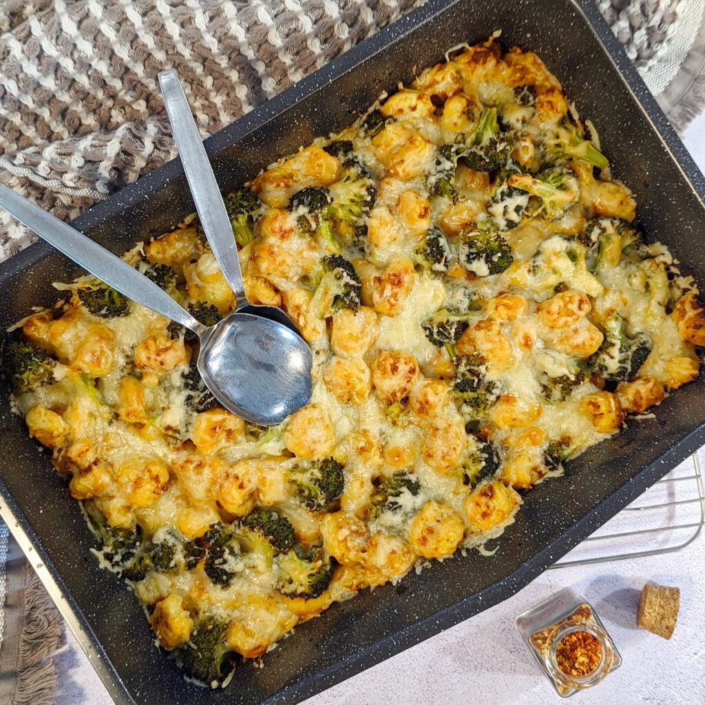 Frisch zubereitete köstliche Gnocchi mit Pesto Rosso und Brokkoli, in einer Auflaufform mit zwei Löffeln, bereit zum Servieren