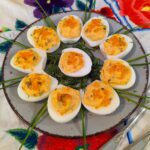 Ein Tablett mit köstlich gefüllten Russian Eggs mit Bacon und Knoblauch, garniert mit frischen Kräutern und rotem Kaviar und serviert auf einem traditionell bestickten Tuch