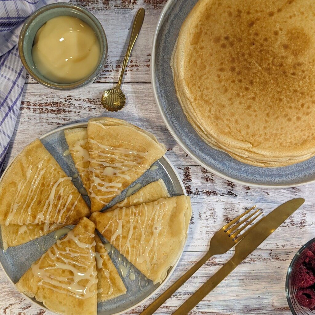 Ein Teller mit traditionellen russischen Blini (Bliny), angerichtet mit gezuckertem Kondensmilch und Himbeeren