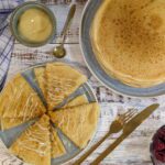 Ein Teller mit traditionellen russischen Blini (Bliny), angerichtet mit gezuckertem Kondensmilch und Himbeeren