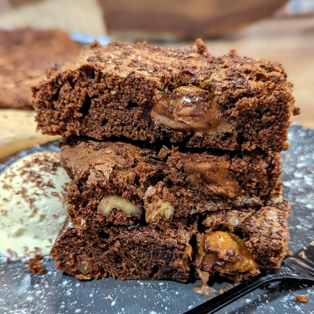 Ein Teller mit frisch gebackenen Schokoladen-Brownies, auf denen Toffifee-Stückchen zu sehen sind, serviert mit einer Kugel Vanilleeis.