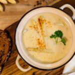 Eine Suppenschüssel mit cremiger Spargelsuppe, garniert mit frischer Petersilie, serviert mit einem Stück Roggenbrot auf einem rustikalen Holztisch.