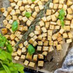 Ein Backblech mit selbstgemachten würzigen Croutons, , verziert mit einem Rosmarinzweig und mehreren Basilikumblättern