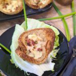 Ein Teller mit golden gebackenem Toastbrot-Käse-Muffins, garniert mit knusprigem Bacon und Frühlingszwiebeln, auf einem rustikalen Holztisch